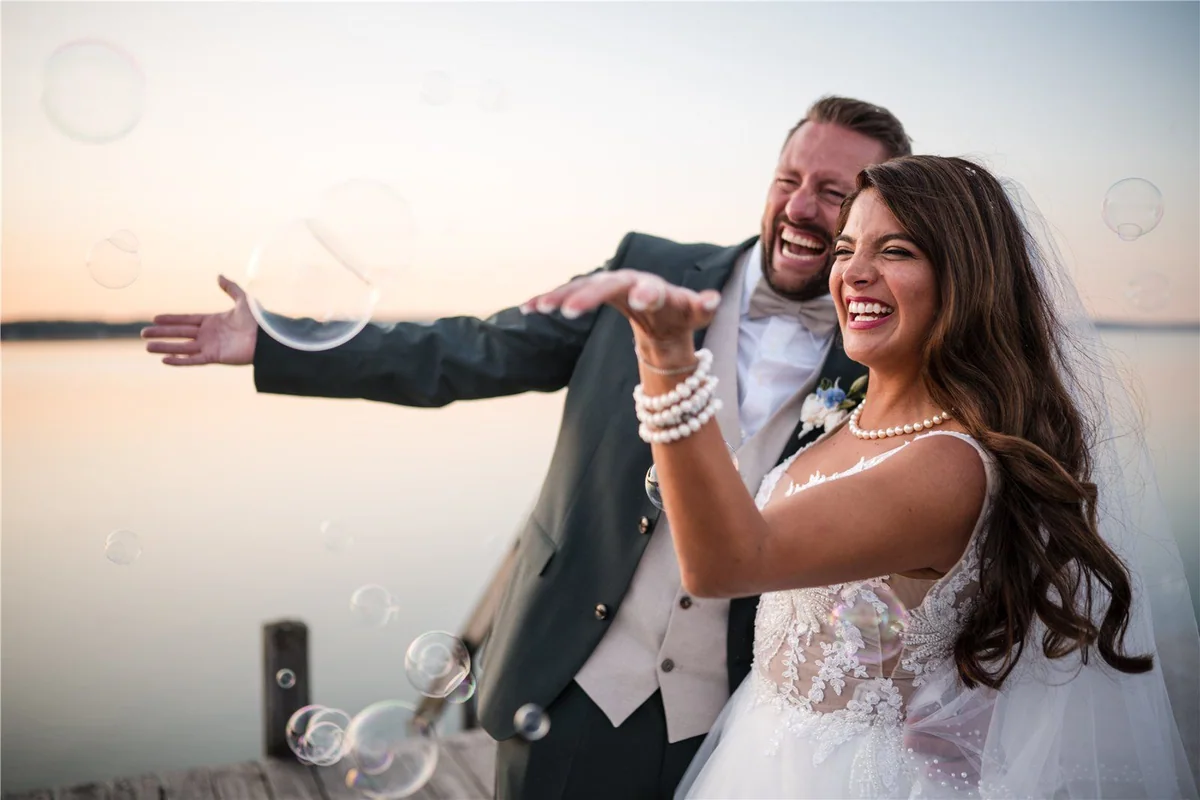 The couple laugh among soap bubbles by the water.