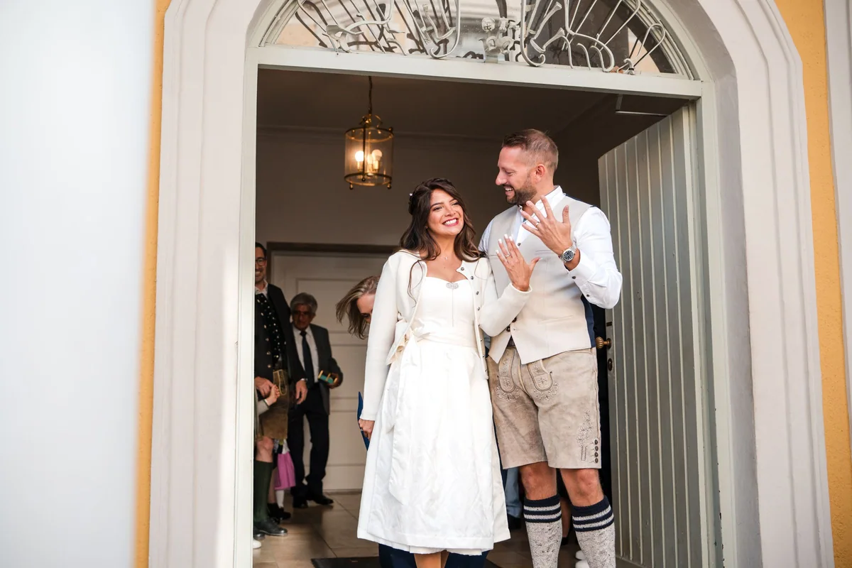 Das Paar in Tracht tritt aus dem Rundbogenportal des Standesamts in der Mandlstraße.