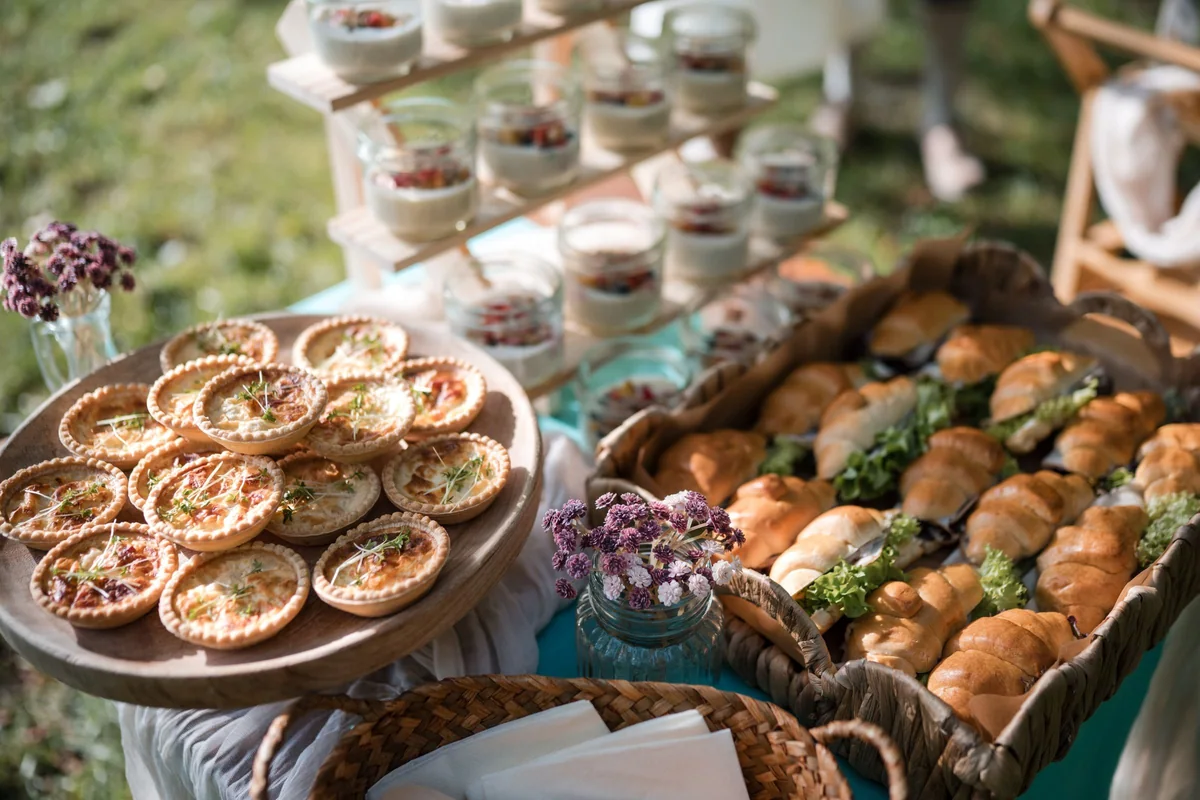 Kleine Tartes und Brötchen auf einem Holztablett im Gras.