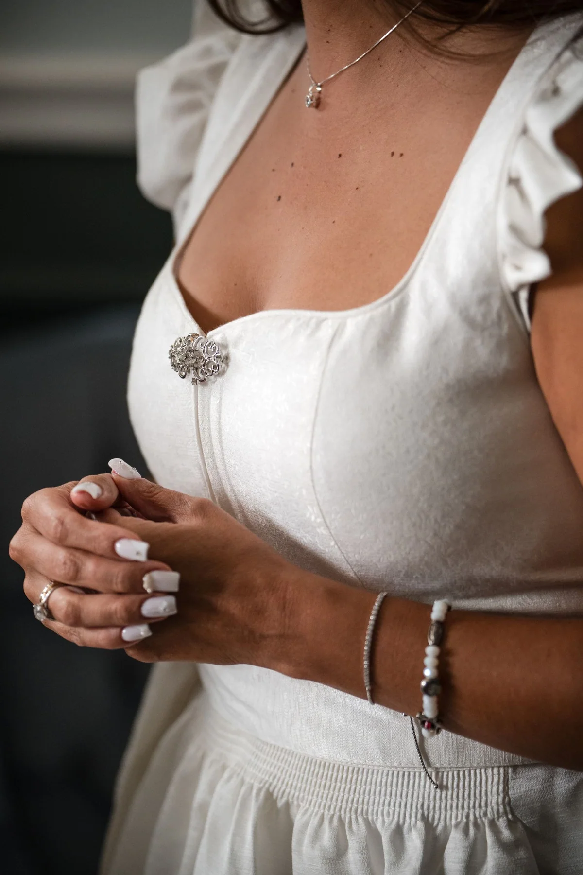 Die Braut im weißen Trachtenkleid faltet die Hände, am Mieder glänzt eine Brosche.