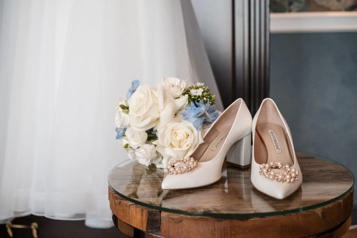 Brautstrauß in Weiß und Hellblau und glitzernde Brautschuhe vor dem Kleid.