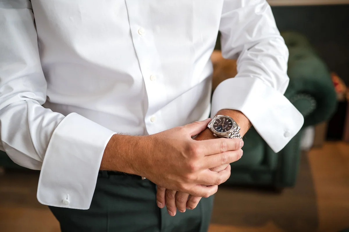Der Bräutigam schließt seine Armbanduhr am weißen Hemd.