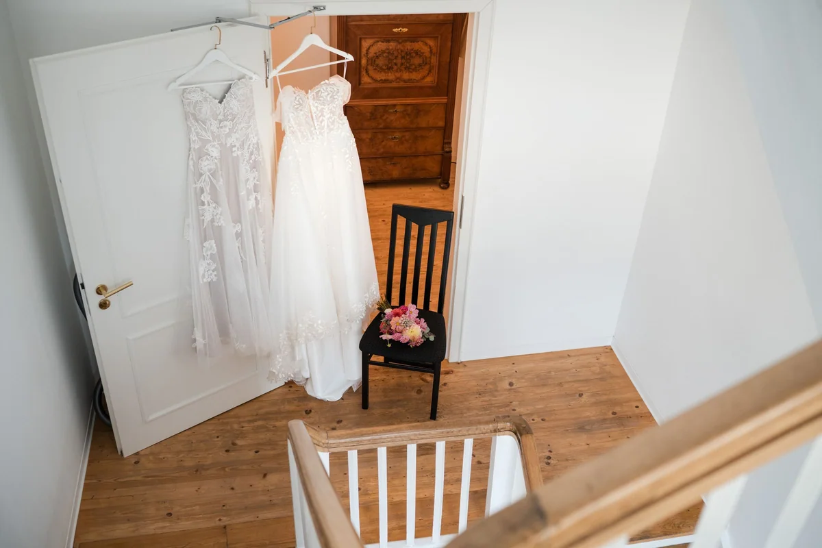 Zwei Brautkleider hängen nebeneinander an einer weißen Tür im Hotelzimmer.