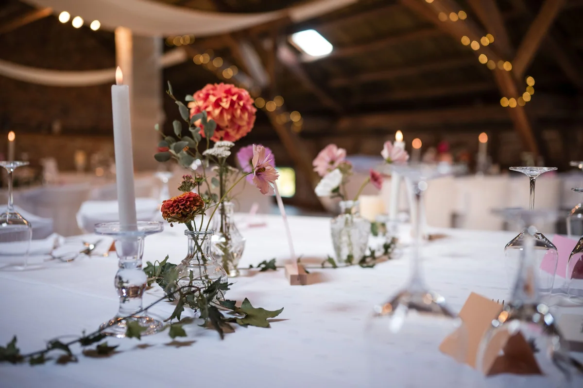 Dahlien in kleinen Glasvasen, Kerzen und Efeu auf einer weißen Tafel.