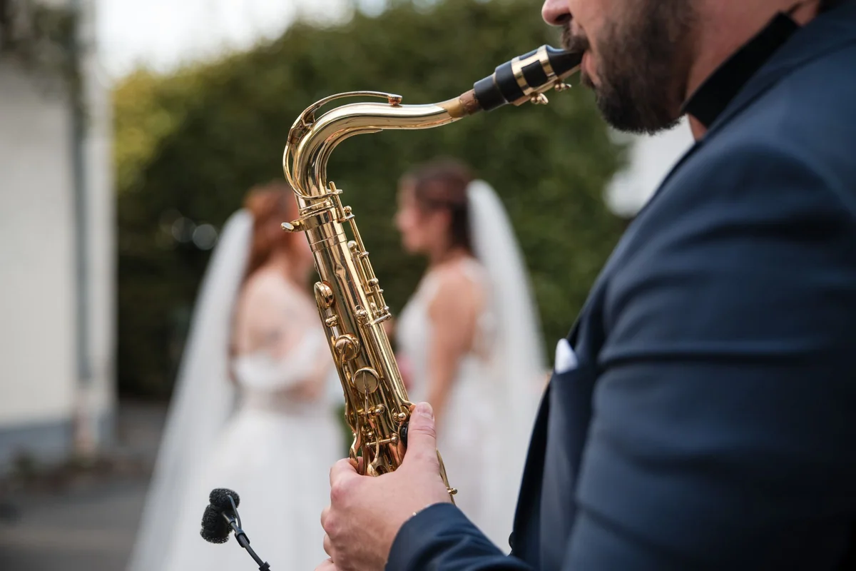 Ein Saxophonist spielt, dahinter tanzen die beiden Bräute.
