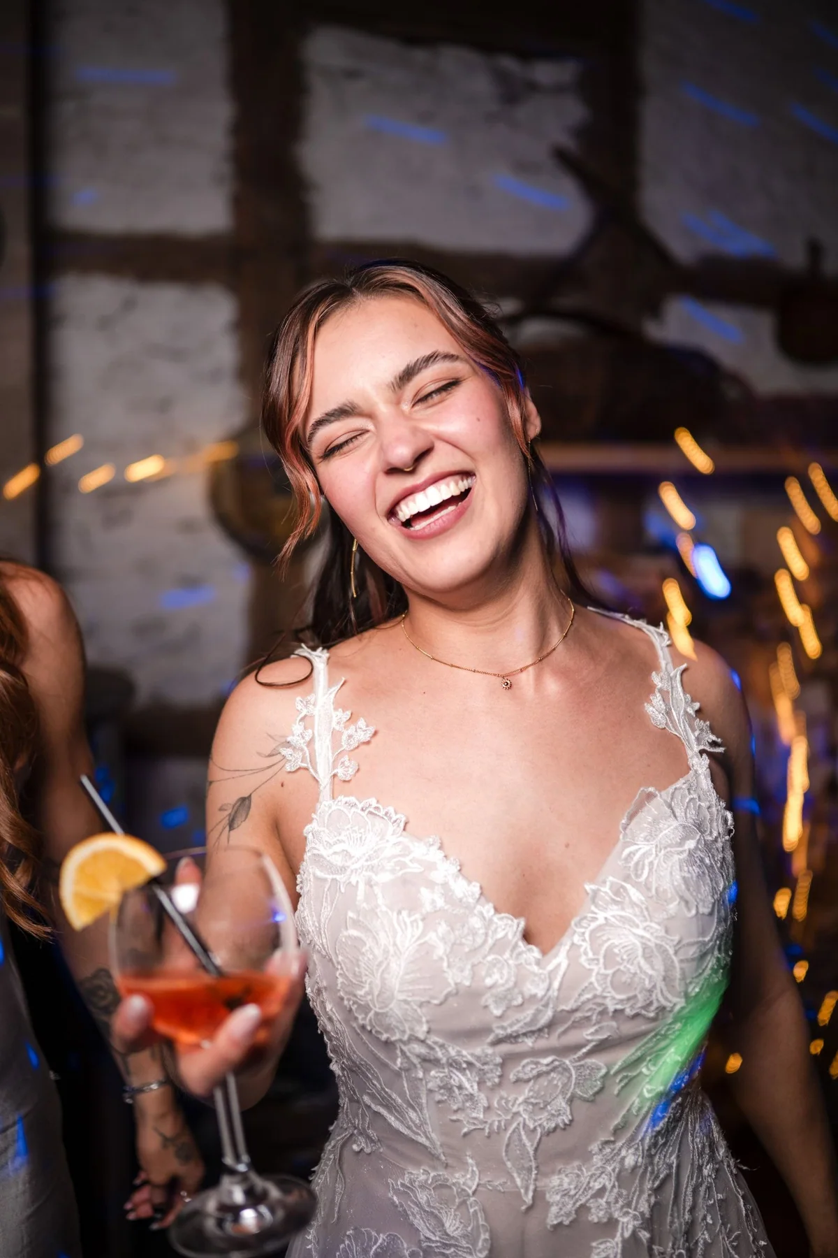 Eine Braut lacht mit einem Drink in der Hand auf der Tanzfläche.