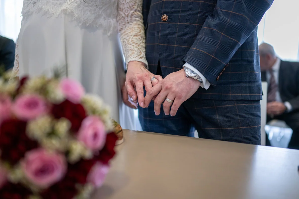 The couple's hands with wedding rings during the ceremony in Linkenheim, the bouquet in front.