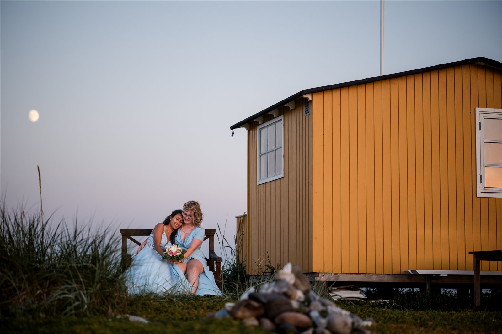 Zwei Menschen sitzen vor einer gelben Strandhütte.